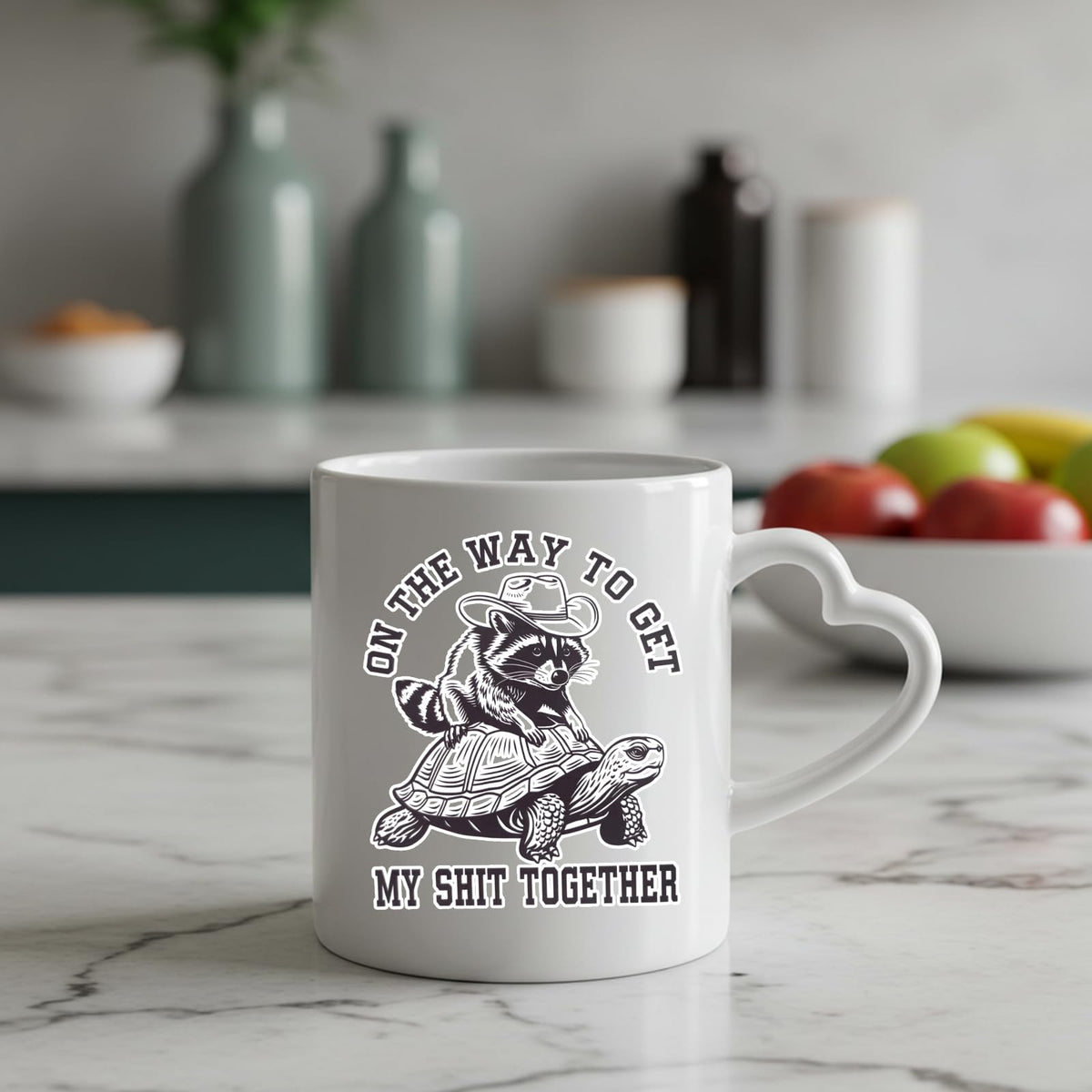 raccoon and tortoise heart-handle mug on a marble counter with fruit