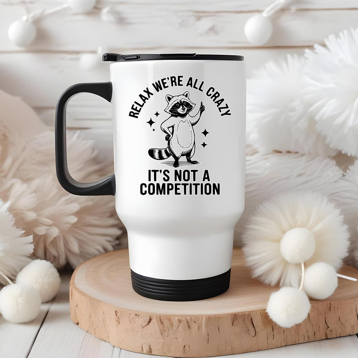 Relax We’re All Crazy raccoon travel mug on a wooden slice with white pom-poms