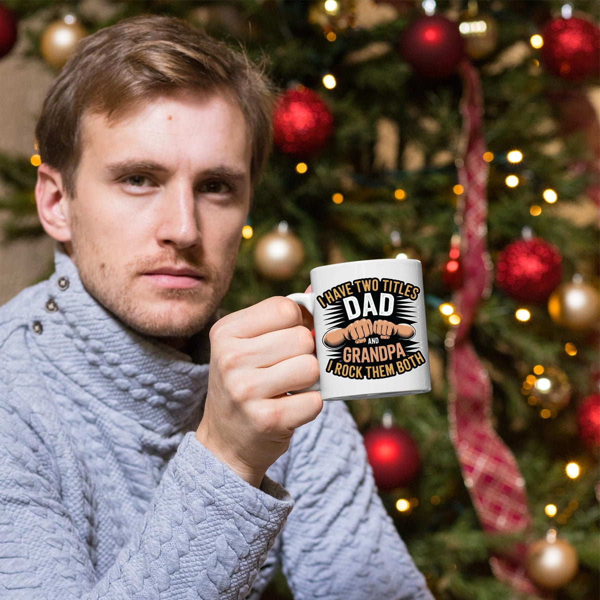Man holding the Two Titles Dad and Grandpa mug in front of a Christmas tree
