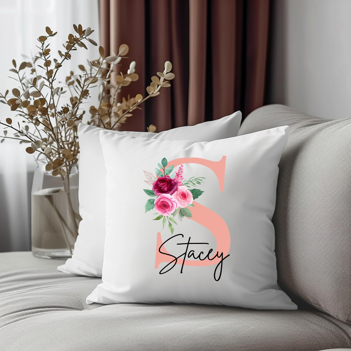 Cushion with a blush pink initial with roses and an example name on a grey sofa