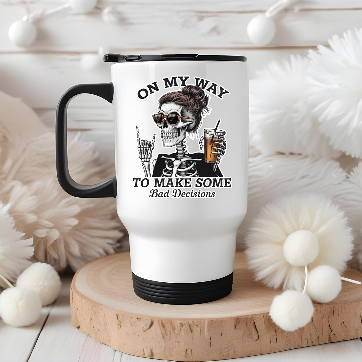 Bad Decisions skeleton travel mug on a wooden slice with white pom-poms