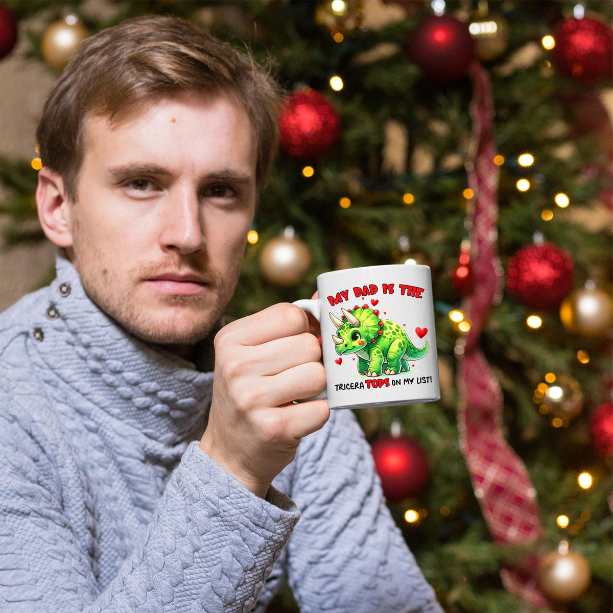 Man holding the Triceratops dad mug in front of a Christmas tree