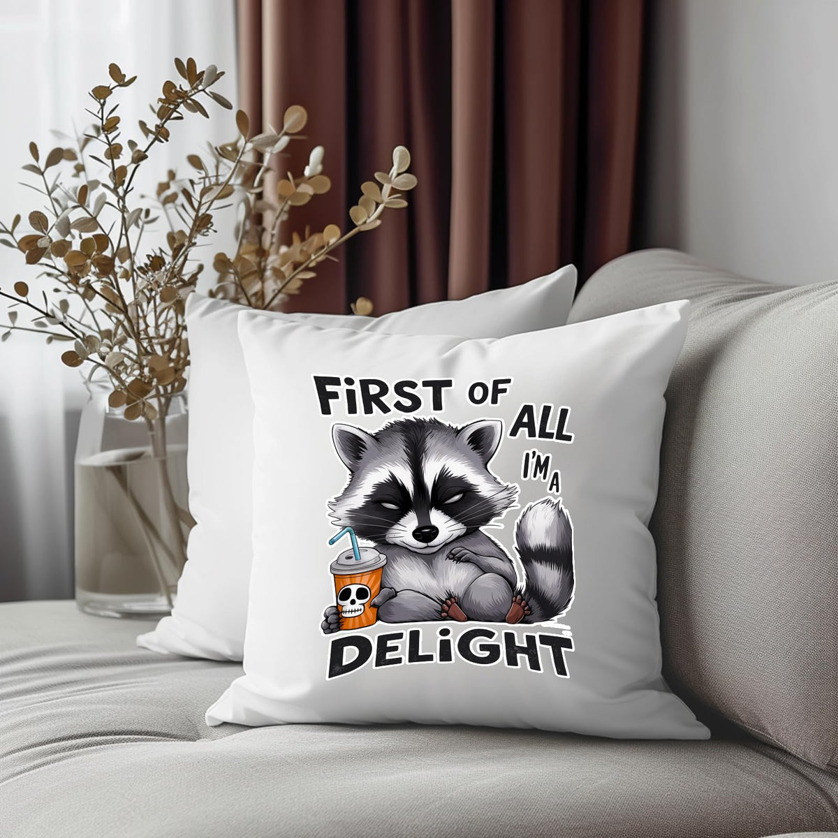 First of All I’m a Delight raccoon cushion on a grey sofa beside dried flowers
