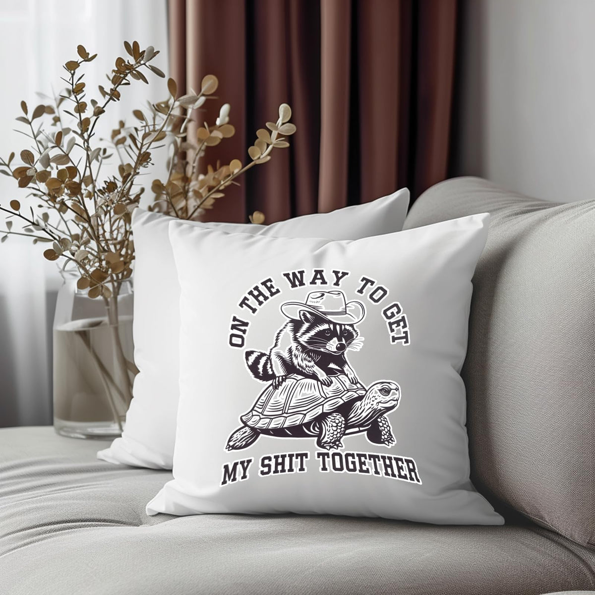 raccoon and tortoise cushion on a grey sofa beside dried flowers