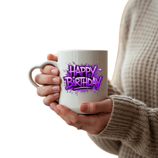 Hands holding the heart-handle mug with purple graffiti “Happy Birthday” lettering