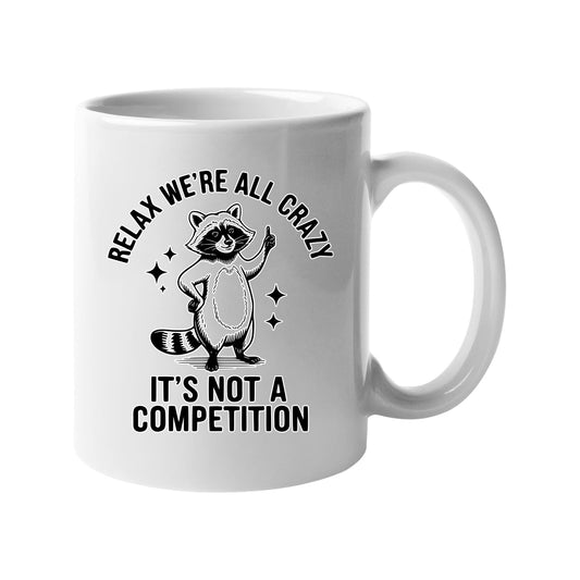 White mug with a raccoon and “Relax, we’re all crazy – it’s not a competition”