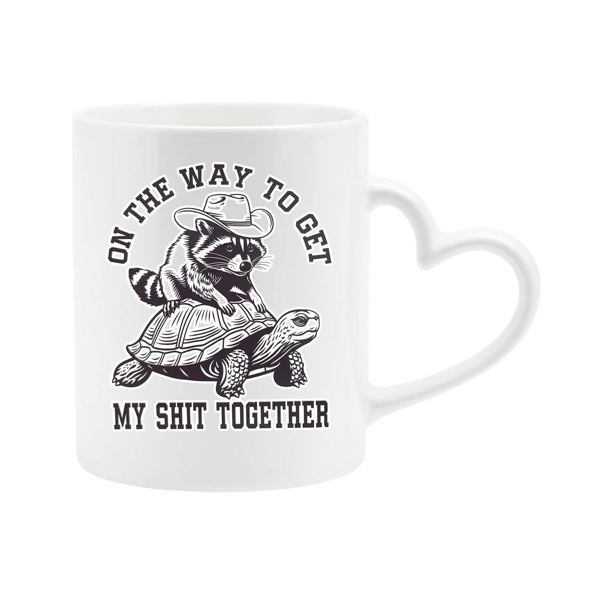 White heart-handle mug with a raccoon in a cowboy hat riding a tortoise and “On the way to get my shit together”