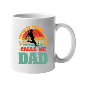 White mug with a footballer in silhouette on a retro sunset with “My favorite soccer player calls me Dad”