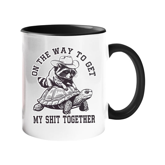 Colour handle mug with a raccoon in a cowboy hat riding a tortoise and “On the way to get my shit together” – black handle and inside