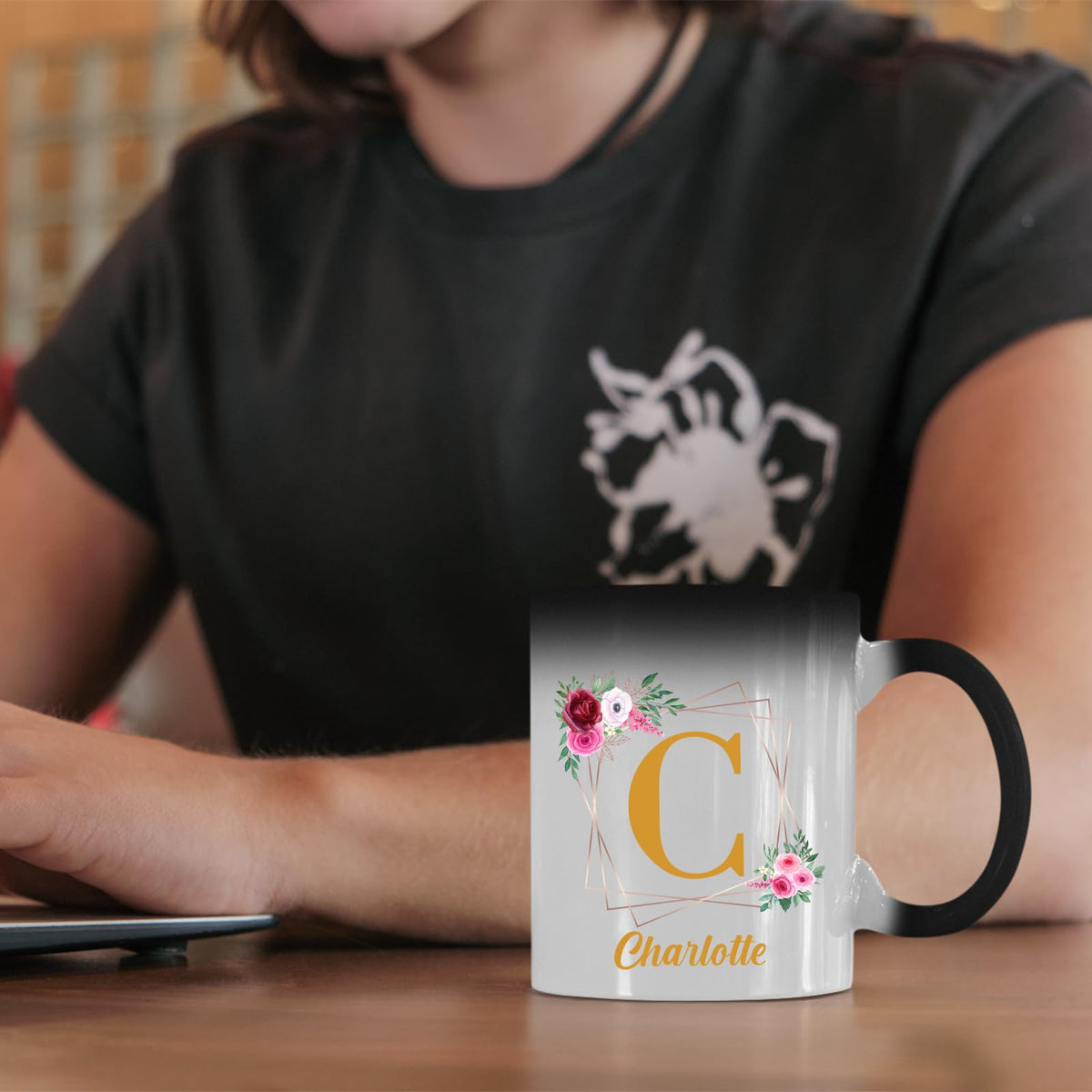Colour changing mug with a gold initial in a floral frame and an example name on a desk