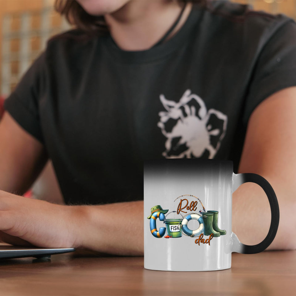 Reel Cool Dad colour changing mug on a desk beside a laptop