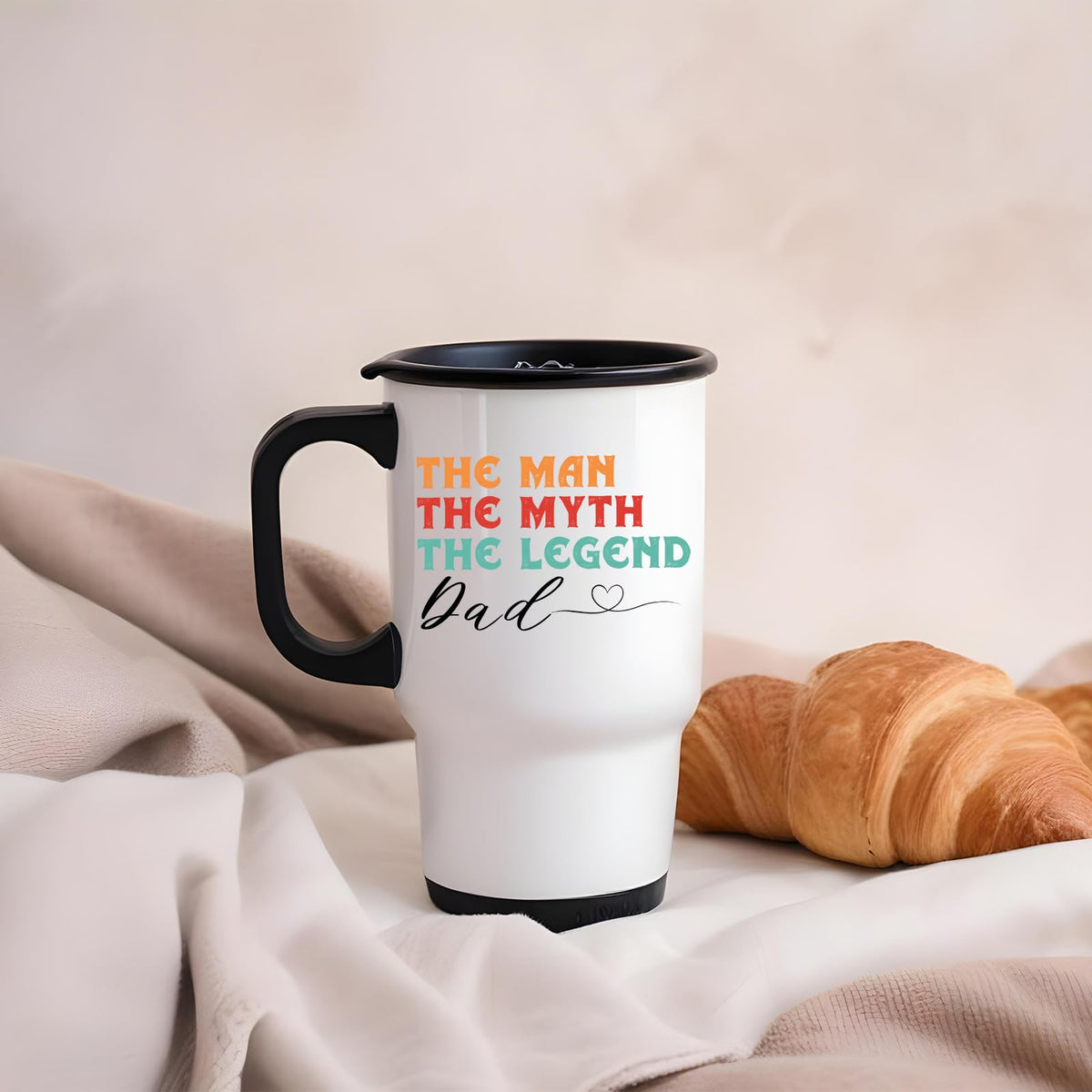 The Man the Myth Dad travel mug on a soft blanket beside a croissant