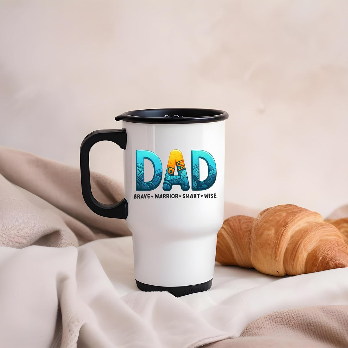 DAD Brave Warrior travel mug on a soft blanket beside a croissant