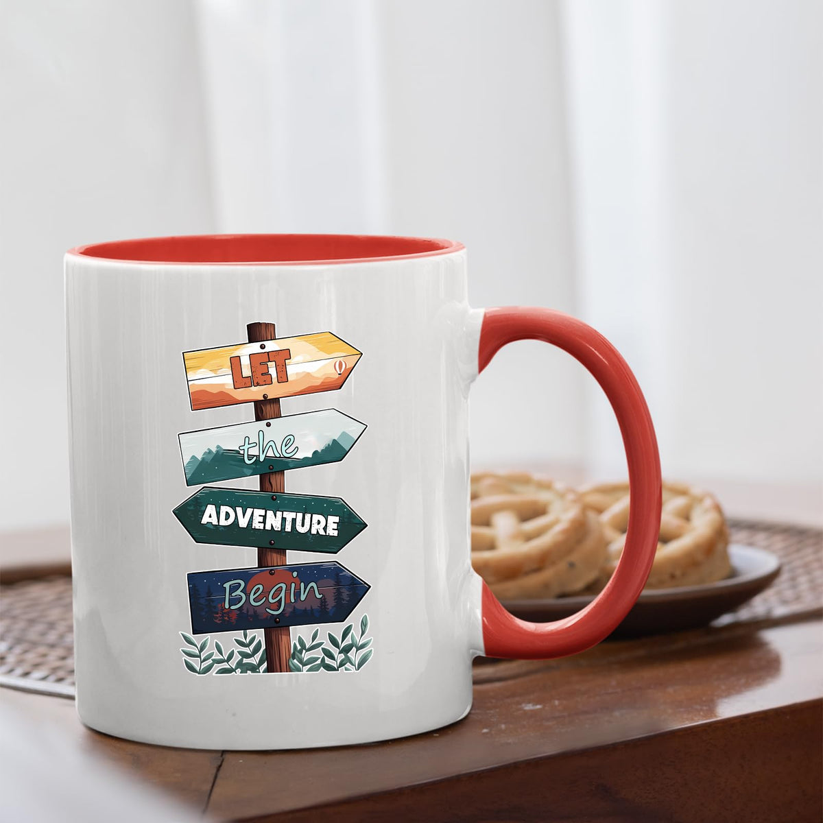 Let the Adventure Begin mug with a red handle beside biscuits