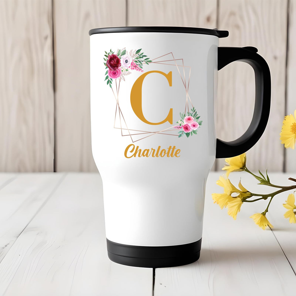 Travel mug with a gold initial in a floral frame and an example name on a white table with yellow flowers