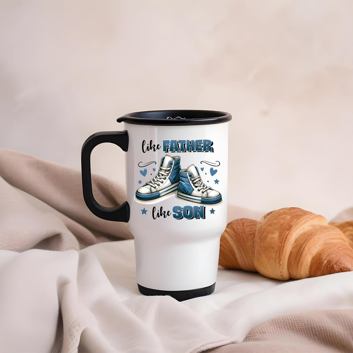 Like Father Like Son travel mug on a soft blanket beside a croissant