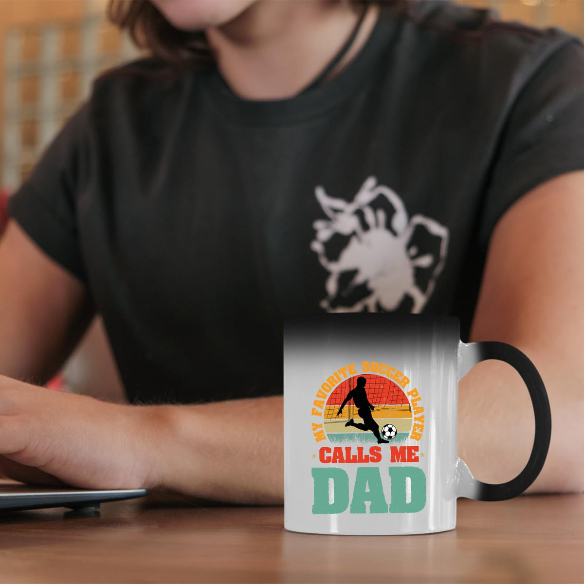 Soccer Dad colour changing mug on a desk beside a laptop