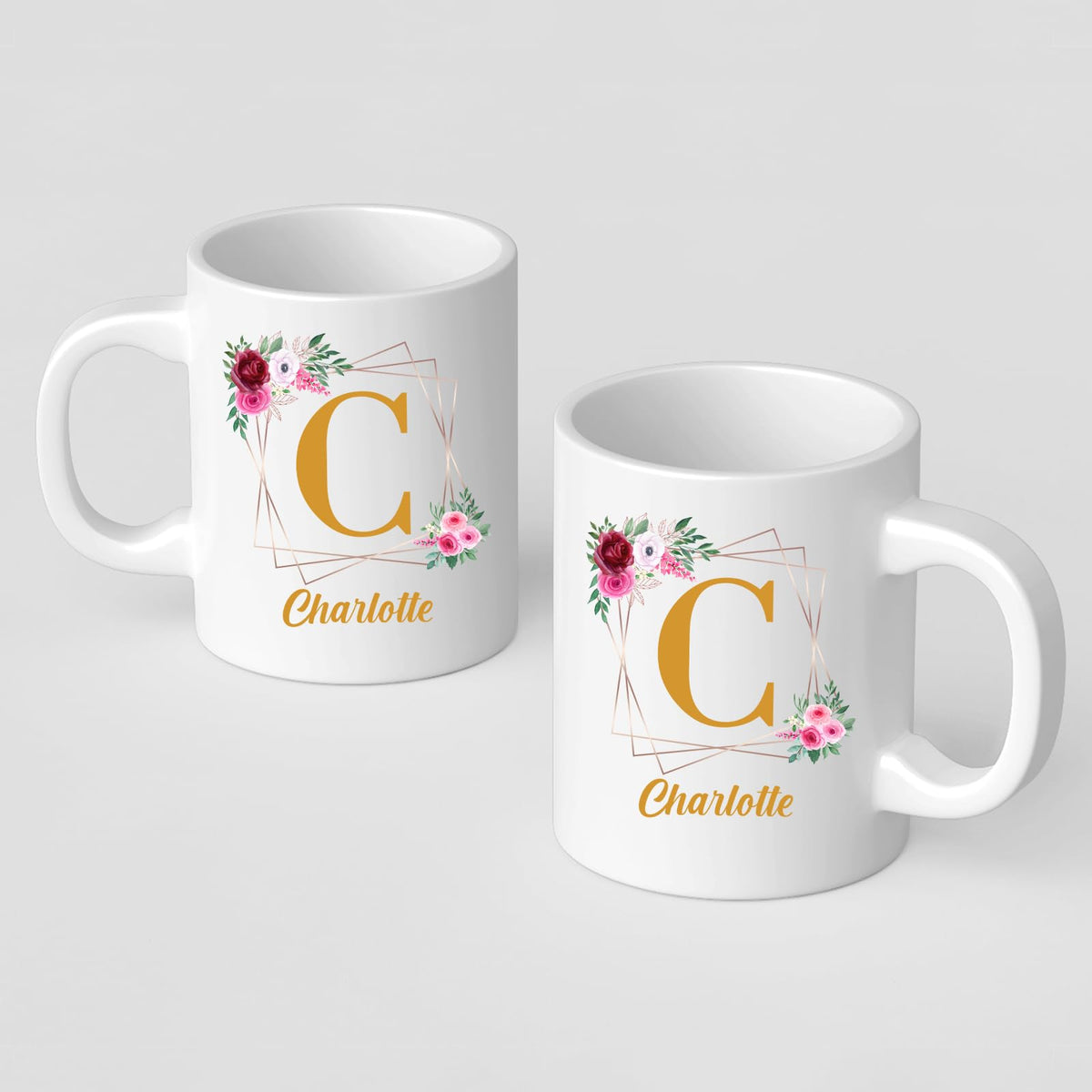 Two white mugs with a gold initial in a floral frame and an example name