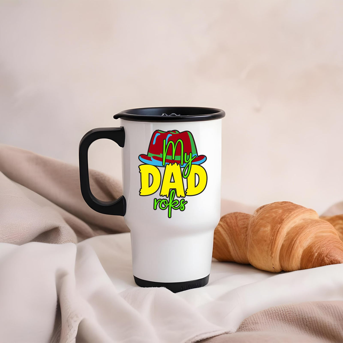 Travel mug with the My Dad Rocks design beside a croissant