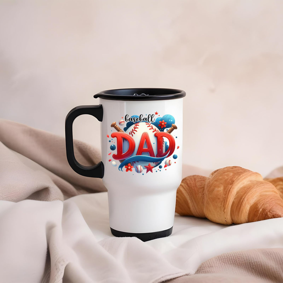 Baseball Dad travel mug on a soft blanket beside a croissant