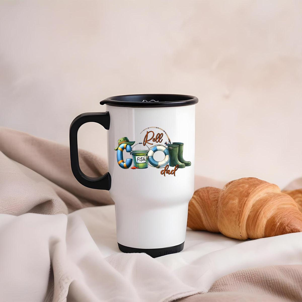 Reel Cool Dad travel mug on a soft blanket beside a croissant
