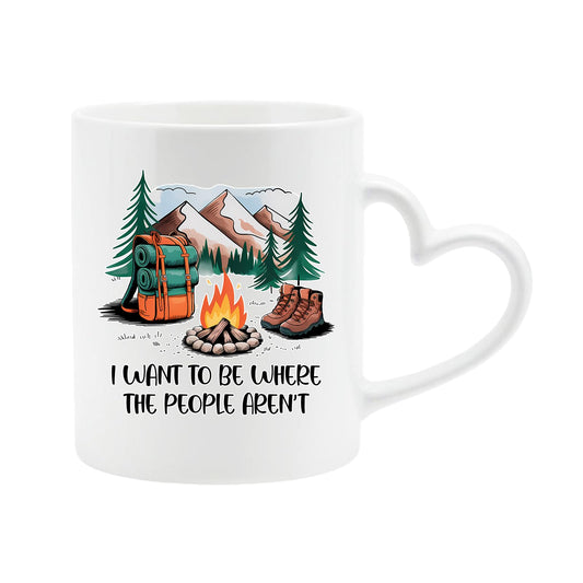 White heart-handle mug with a campfire, backpack, boots and mountains with “I want to be where the people aren’t”