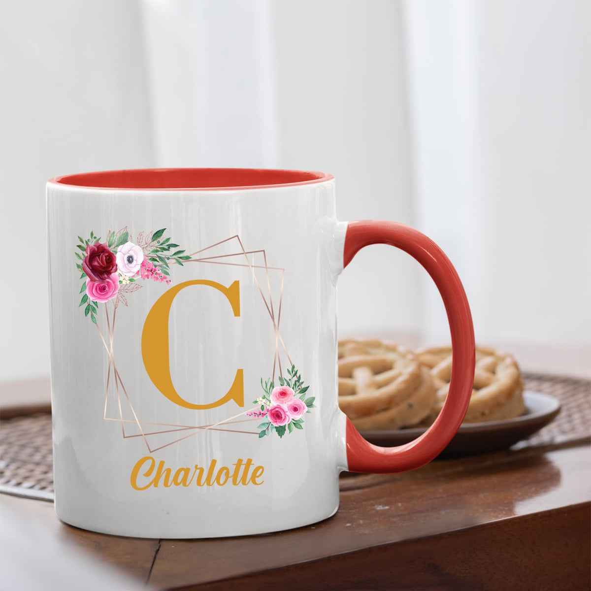 Red handle mug with a gold initial in a floral frame and an example name on a table