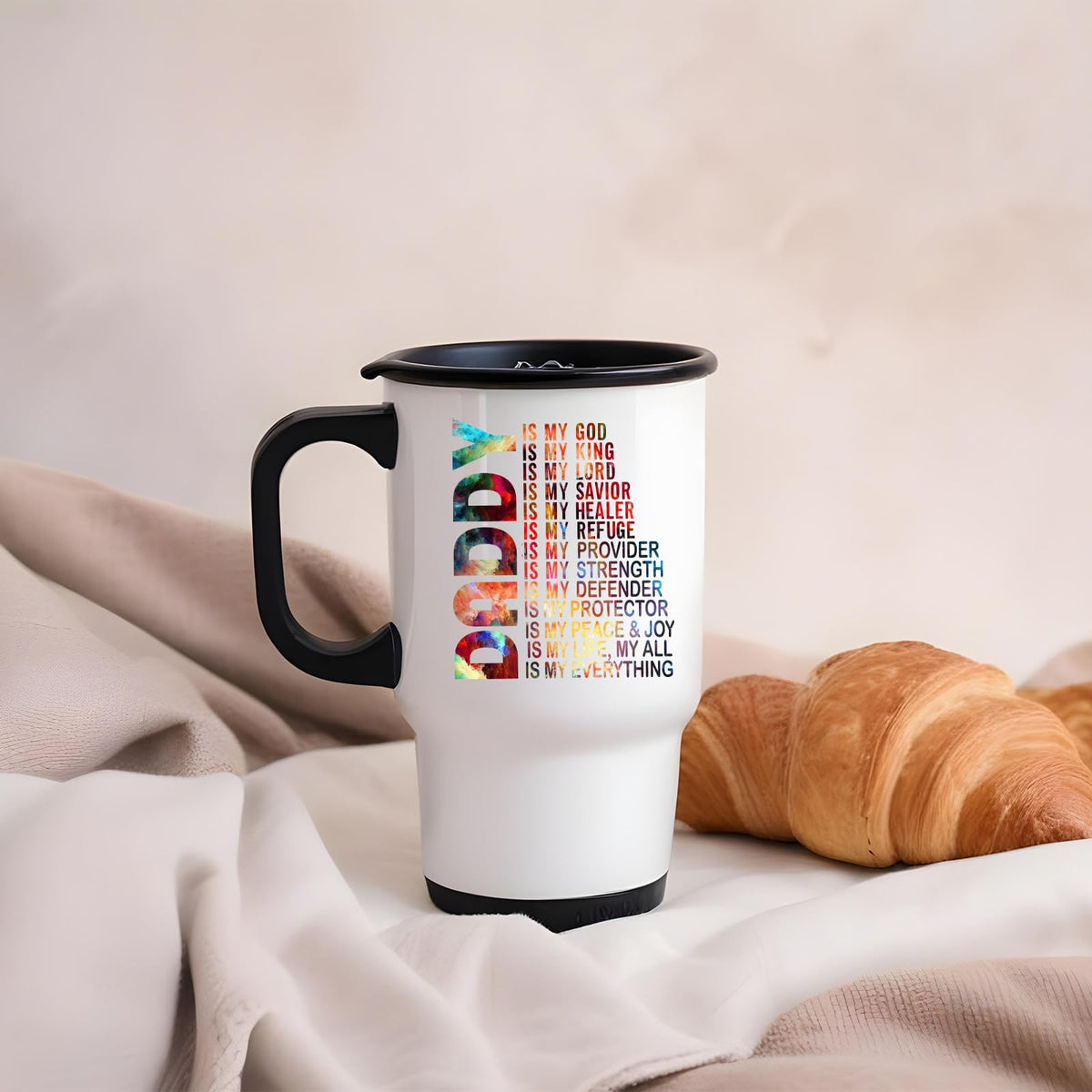 Daddy Is My God travel mug on a soft blanket beside a croissant