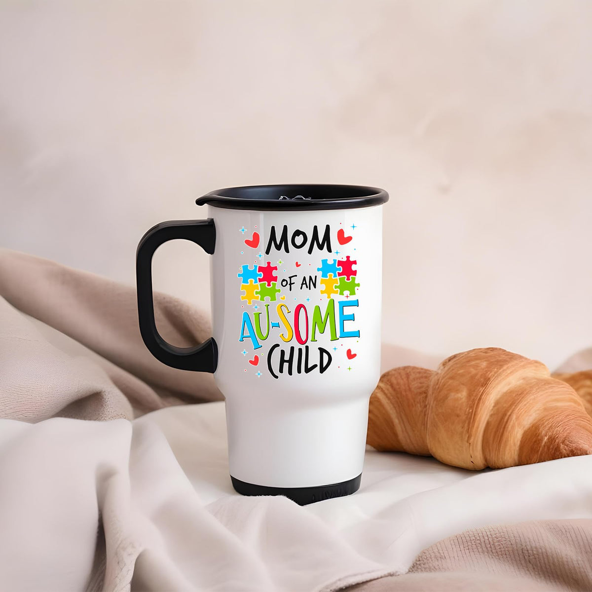 Mom of an Au-Some Child travel mug on a soft blanket beside a croissant
