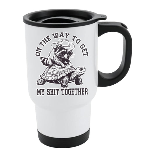White travel mug with black lid and a raccoon in a cowboy hat riding a tortoise and “On the way to get my shit together”