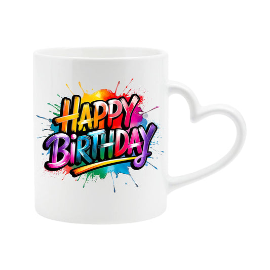 White heart-handle mug with “Happy Birthday” in bold rainbow letters on a colourful paint splash