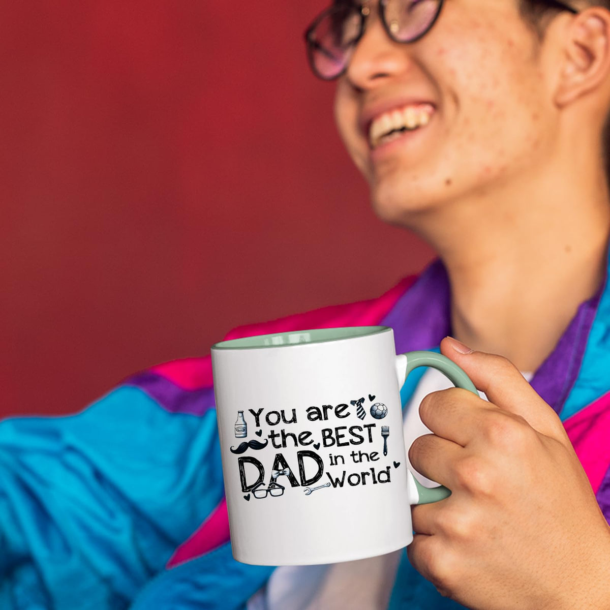 Smiling person in a colourful jacket holding the Best Dad in the World sketch mug with a light green handle