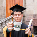 Graduate in cap and gown holding the Reel Cool Dad mug