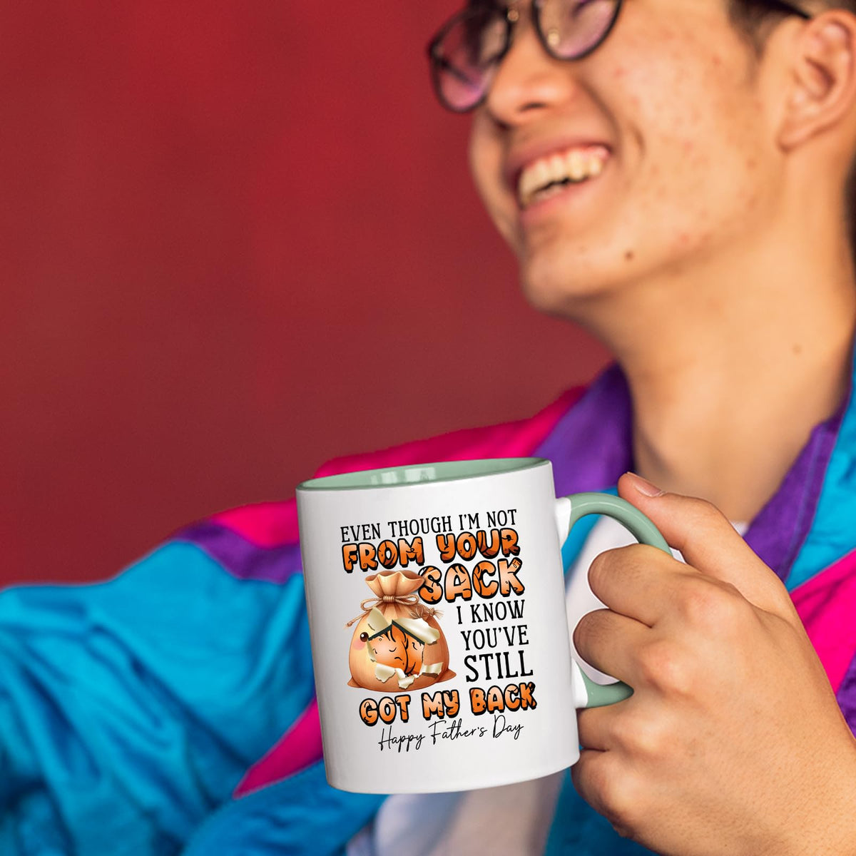 Smiling person in a colourful jacket holding the Not From Your Sack mug with a light green handle