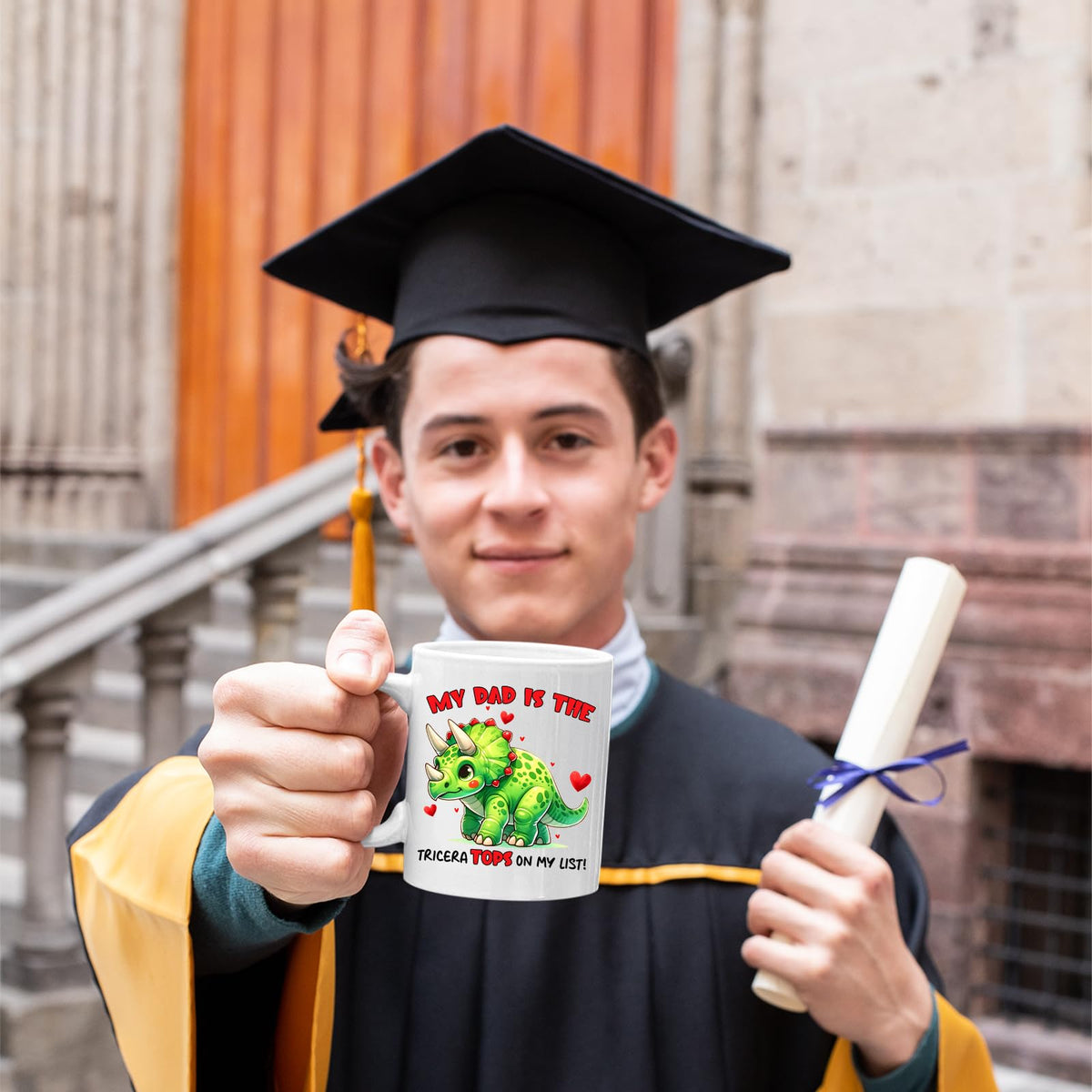 Graduate in cap and gown holding the Triceratops dad mug