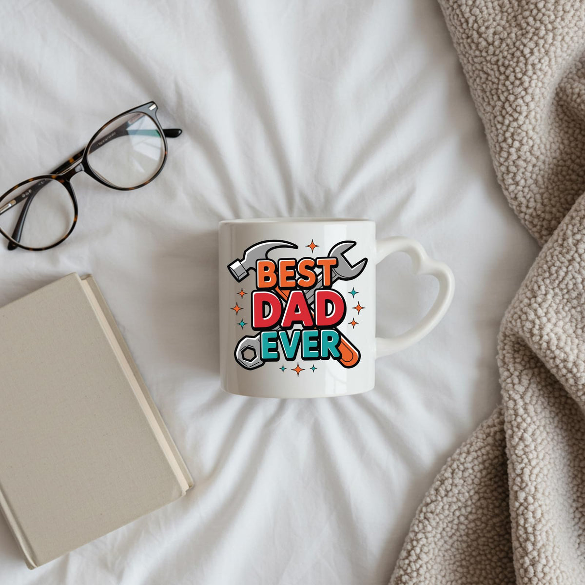 Best Dad Ever tools heart-handle mug on a bed beside glasses and a book