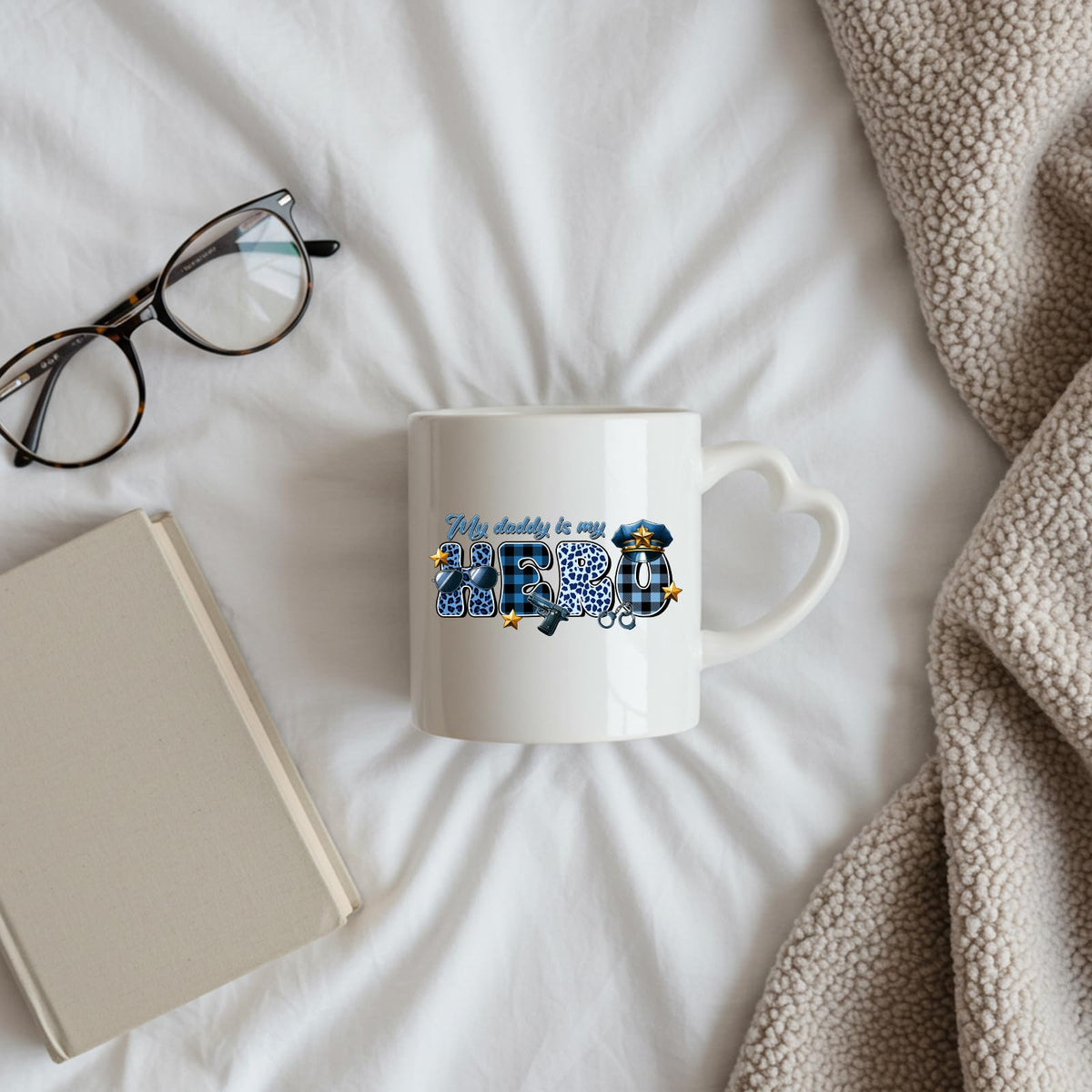 My Daddy Is My Hero police heart-handle mug on a bed beside glasses and a book