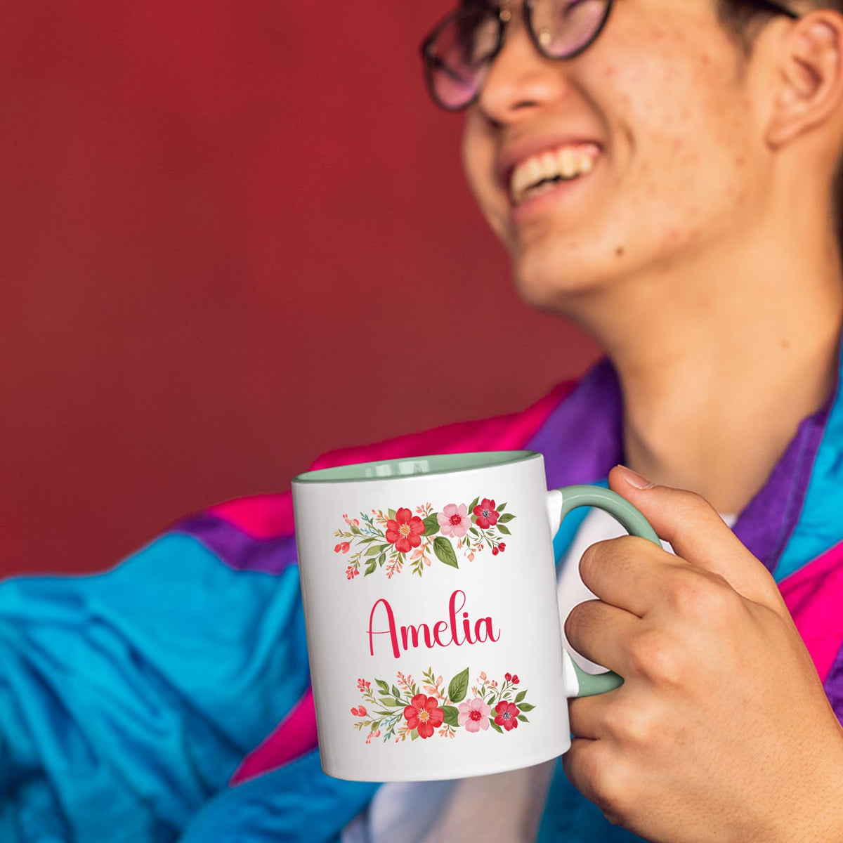 Person laughing while holding a lime handle mug with a red flower border around an example name