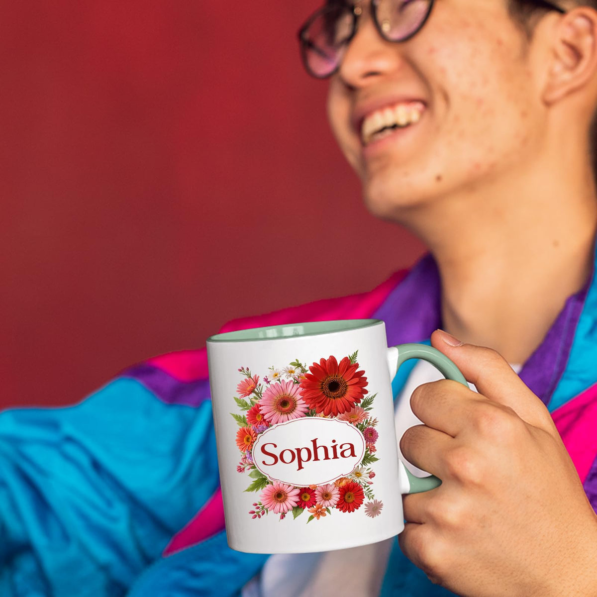 Person laughing while holding a lime handle mug with a red gerbera wreath around an example name
