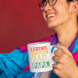Smiling person in a colourful jacket holding the Legend Husband Dad Papa mug with a light green handle