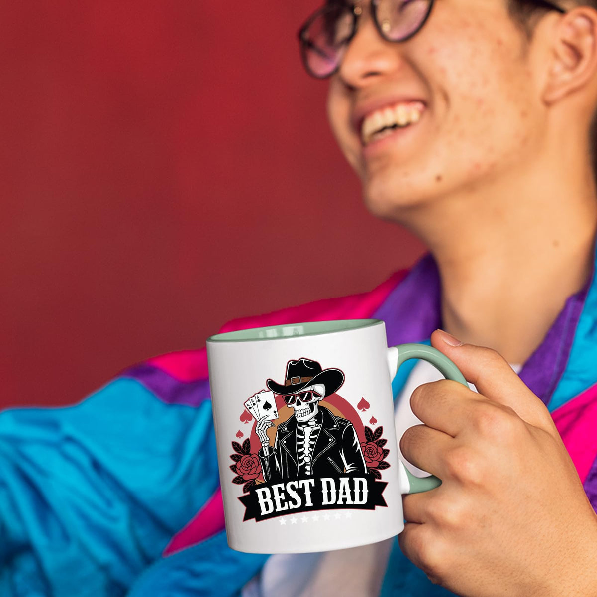 Smiling person in a colourful jacket holding the Best Dad skeleton cowboy mug with a light green handle