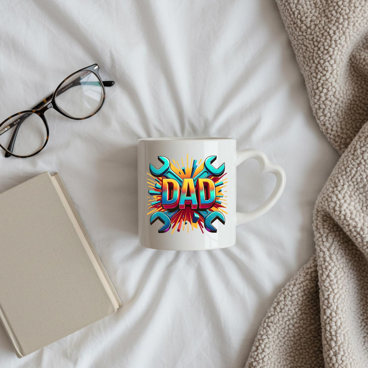 DAD spanners heart-handle mug on a bed beside glasses and a book