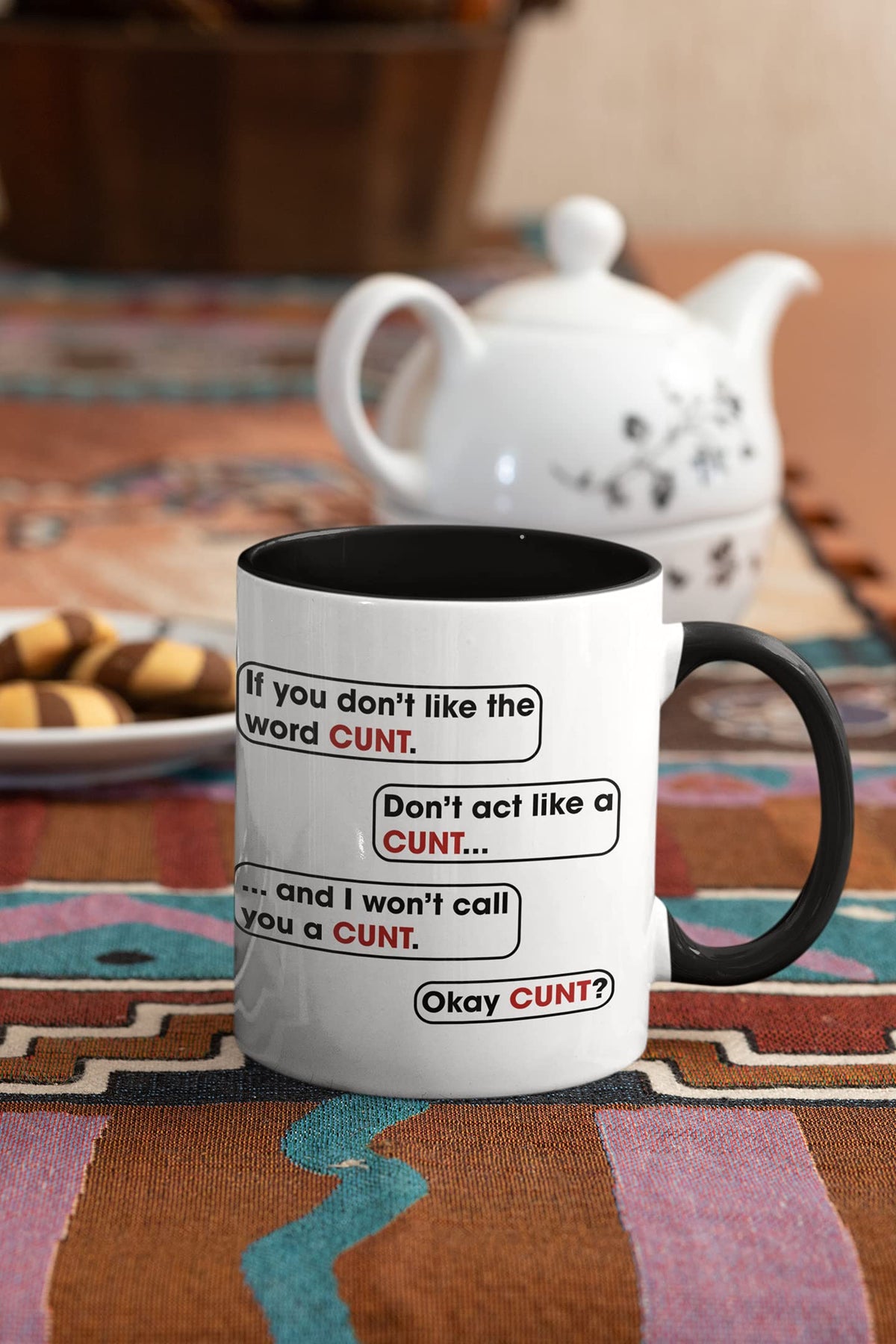 Rude speech bubble mug next to a teapot and biscuits