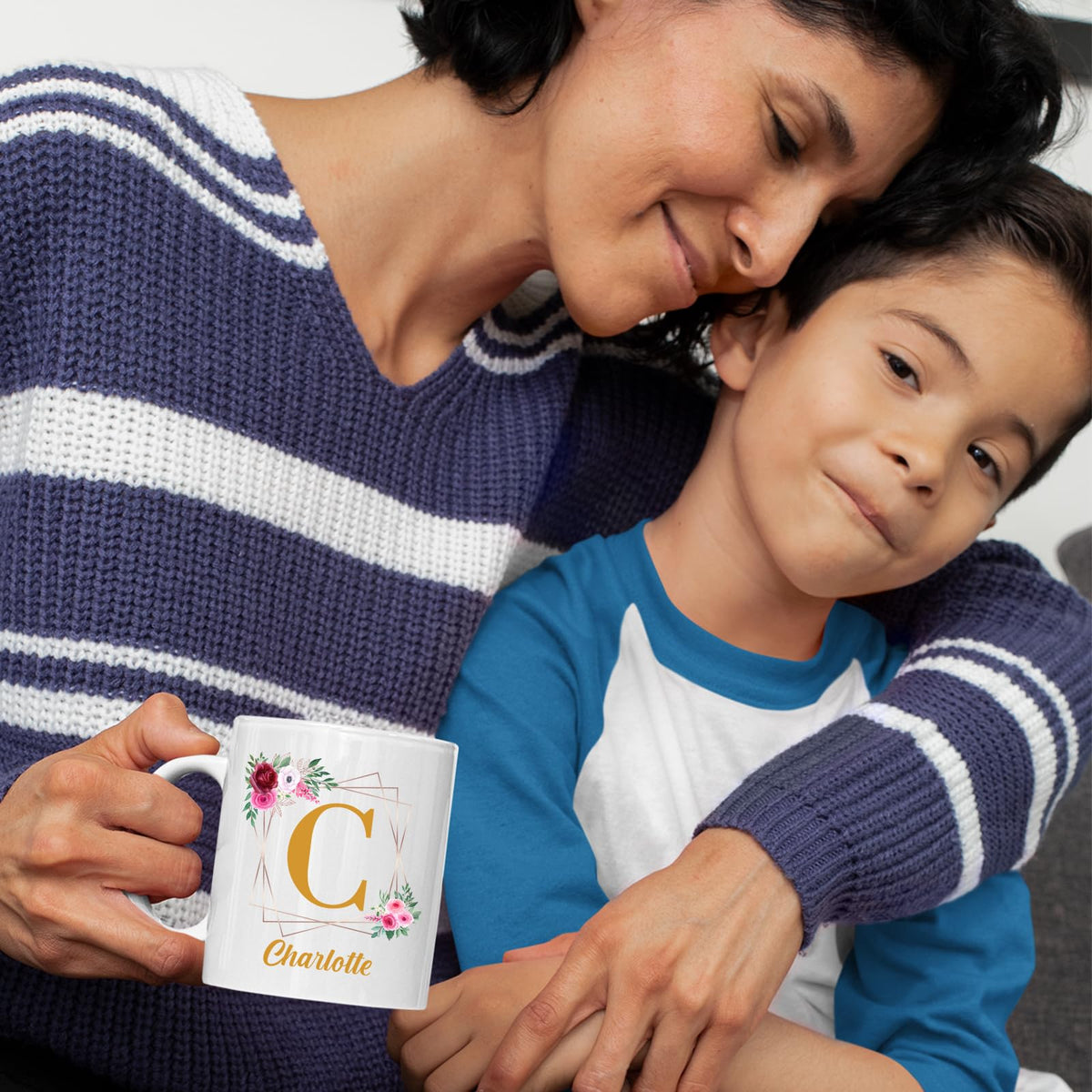 Mother and son cuddling with a mug with a gold initial in a floral frame and an example name