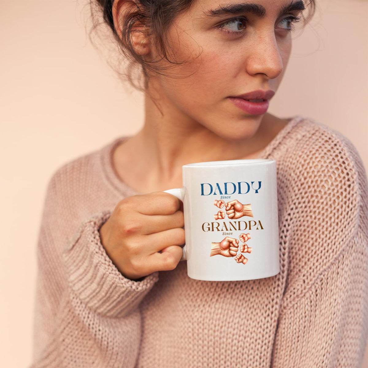 Woman in a pink jumper holding the Daddy and Grandpa fist bump mug