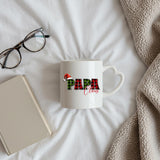 Papa Claus heart-handle mug on a bed beside glasses and a book
