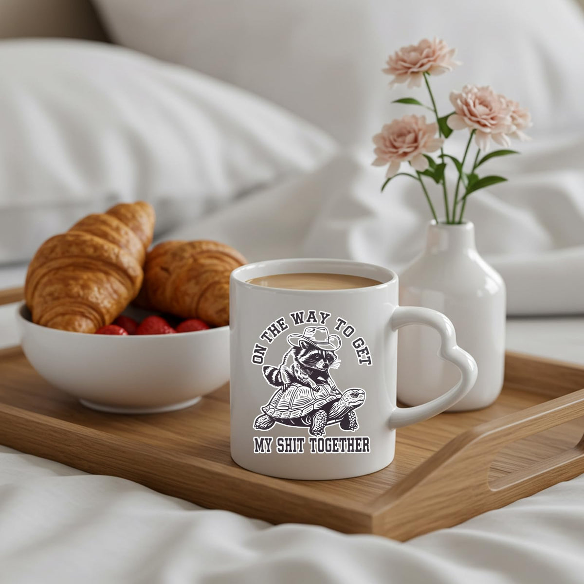 raccoon and tortoise heart-handle mug on a breakfast tray with croissants and flowers
