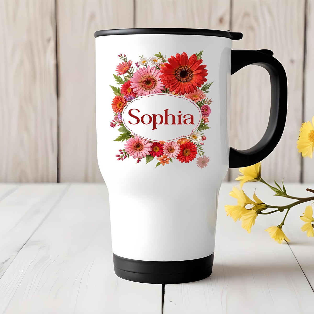 Travel mug with a red gerbera wreath around an example name on a white table with yellow flowers