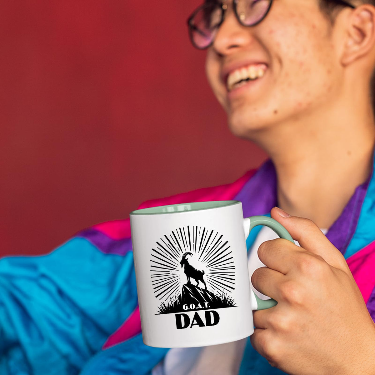 Smiling person in a colourful jacket holding the GOAT Dad mug with a light green handle