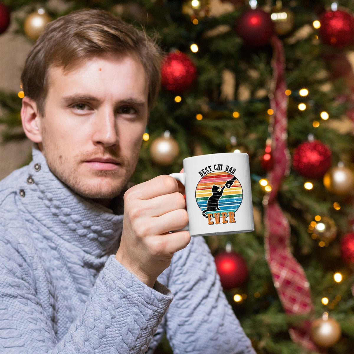 Man holding the Best Cat Dad Ever mug in front of a Christmas tree